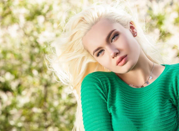 Outdoors portrait of beautiful & positive young blond girl in stylish green sweater. Person against nature.