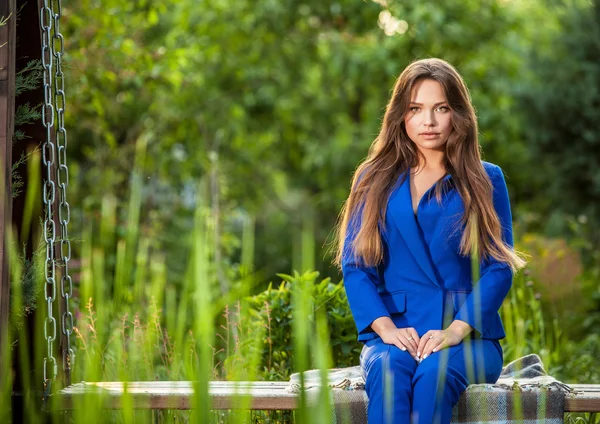 Attractive young woman in official blue suit poses in summer garden.