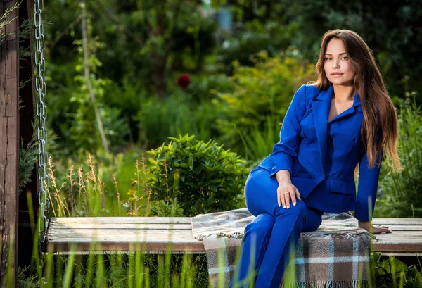 Attractive young woman in official blue suit poses in summer garden.