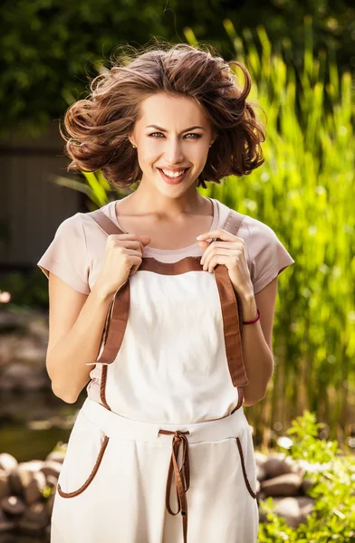 Outdoors portrait of positive young woman in overalls which posing in solar summer garden.