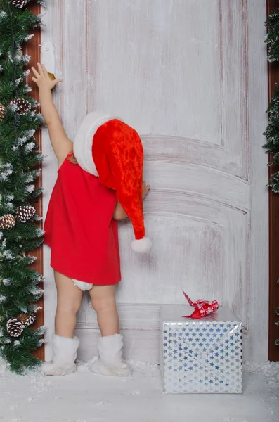 Child dressed as Santa with gift opens door