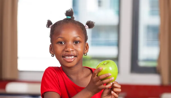 Arican girl at primary school holding green apple in classroom