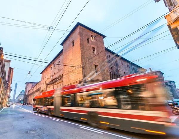 Red bus speeding up in Bologna streets at dusk