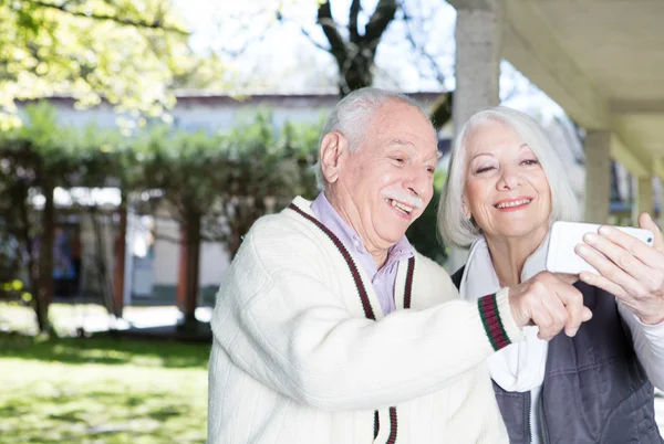 Happy elder couple in 70s outdoor with technology gadget