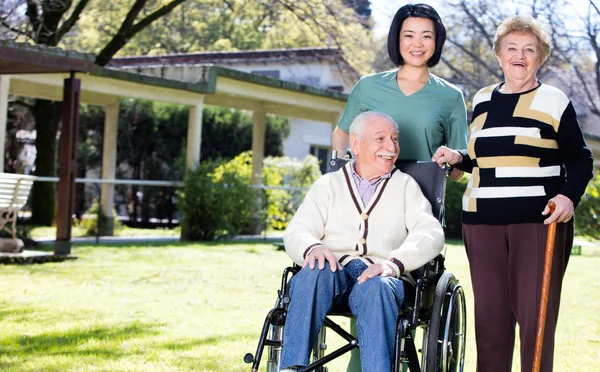 Elder people in rehab facility garden with nurse