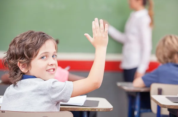 Happy primary school boy raising his hand in the classroom