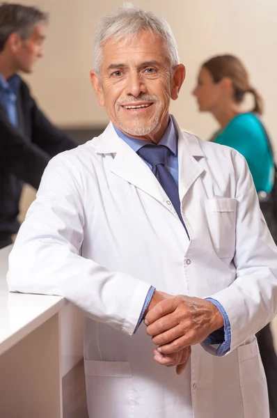 Confident smiling mature male doctor in hospital waiting room