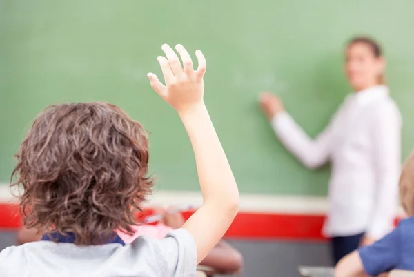 Raising hand at class lesson, primary school scene. Success and
