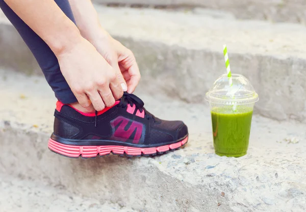 Green detox smoothie cup and woman lacing running shoes before w