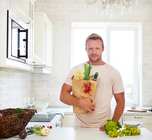 Man holding paper bag full of groceries on the kitchen
