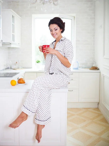 Happy woman holding a cup of coffee wearing pajamas