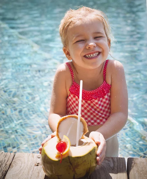 Cute funny little girl drinking coconut at the pool