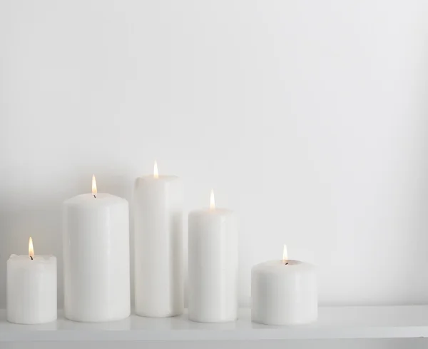 White candles burning on a white shelf