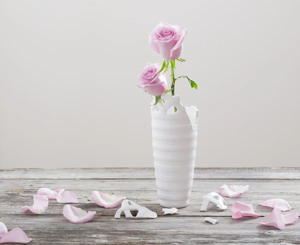 Pink roses in  broken  flower vase on old wooden table