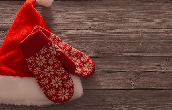 Santa's hat and red mitten on old wooden background