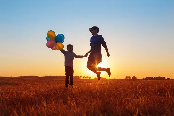 Happy mother and son jumping with balloons outdoor