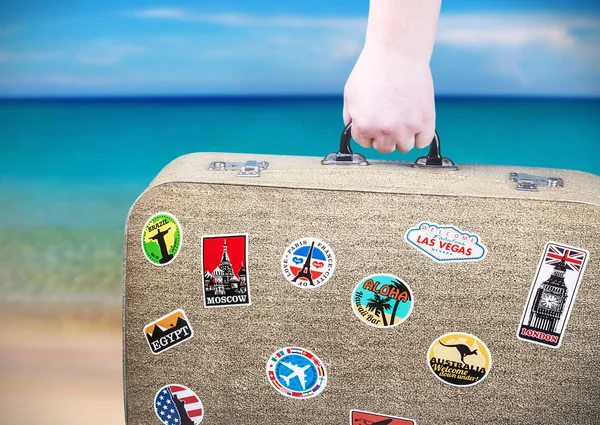 Hand holds a suitcase with stickers