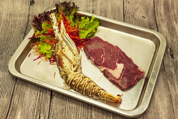 Set for surf and turf a fresh crude lobster and a juicy piece of a marble stake on a tray.