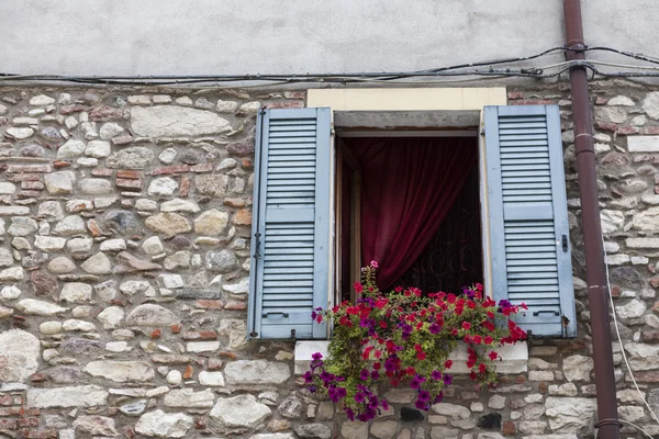 Old window with open shutters with flowers on the window sill on the stone wall. Italian Village