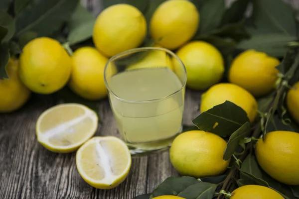 Fresh juicy lemons and a glass of homemade lemonade on a wooden background