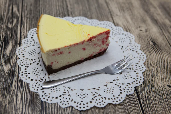 Fresh tasty sweet piece of cheesecake on a white napkin and a dessert fork on a wooden background