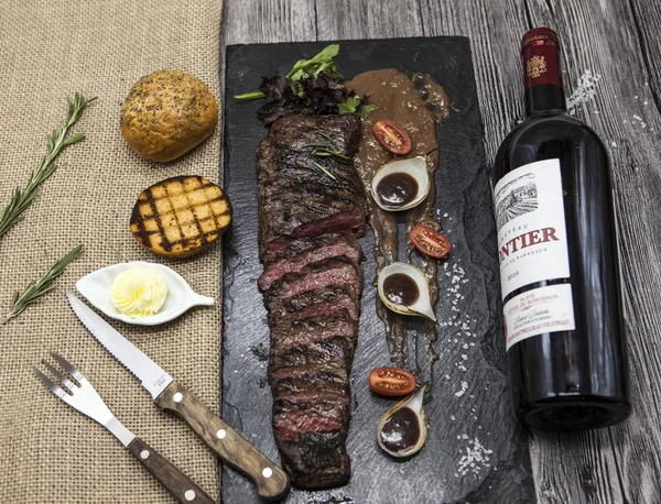 Delicious juicy hot roast beef cut into delicious pieces of meat and vegetables. Served on a black stone plate with a fork and knife and pepper and wine