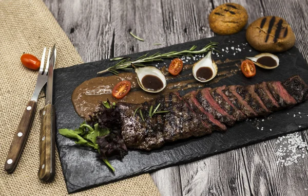 Delicious juicy hot roast beef cut into delicious pieces of meat and vegetables. Served on a black stone plate with a fork and knife and pepper.