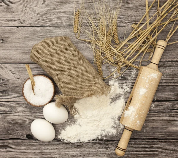 Wheat flour in a canvas bag, with spikelets of rye, a large salt shaker wood, raw eggs, a wooden rolling pin: set for making homemade bread dough on a beautiful dark wooden background