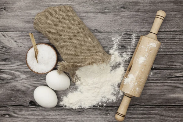 Wheat flour in a canvas bag, a large salt shaker wood, raw eggs, a wooden rolling pin: set for making homemade bread dough on a beautiful dark wooden background