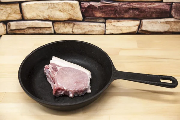 A piece of delicious fresh raw pork close-up on a cast iron skillet on the table rustic kitchen.