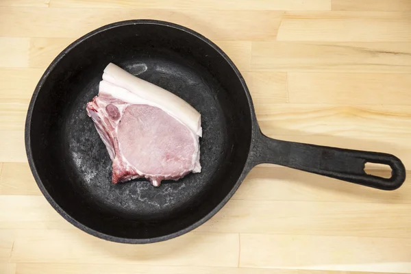 A piece of delicious fresh raw pork close-up on a cast iron skillet on the table rustic kitchen