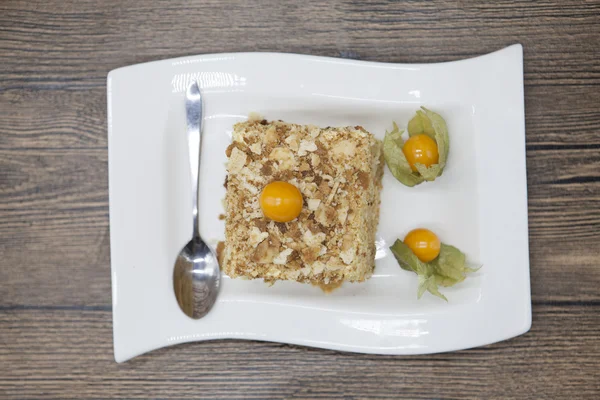 Fresh delicious diet cake with berry Physalis at Dukan Diet on a porcelain plate with a spoon on a wooden background.