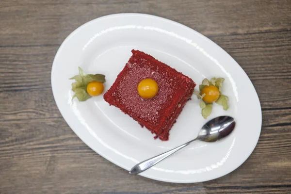 Red Velvet, fresh delicious diet cake with berry Physalis at Dukan Diet on a porcelain plate with a spoon on a wooden background