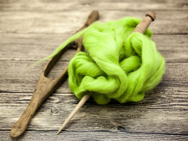 Green wool and old spindle close-up on wooden background. Tools for knitting of wool