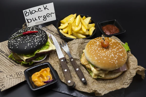 Set of the black burger and classical American burger . Black burger roll slices of juicy marble beef, fused cheese, fresh salad with French fries on a cast-iron griddle, with chili sauce and guakomol