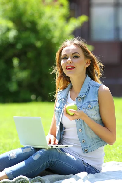 Young girl sitting on the grass with laptop