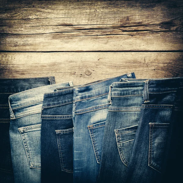 Different jeans on wooden background in store. Retro toned.