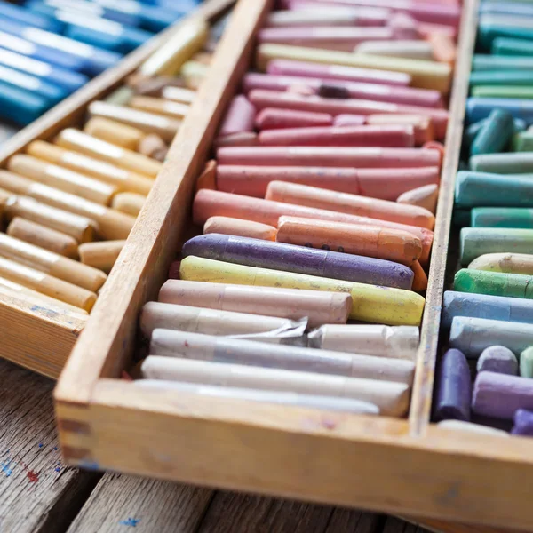 Set of multicolored pastel crayons in open wooden artist box on