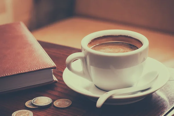 Vintage stylized photo of coffee cup, diary and coins on table i