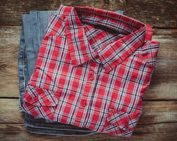 Plaid shirt and pair of jeans on wooden background. Top view. Vi