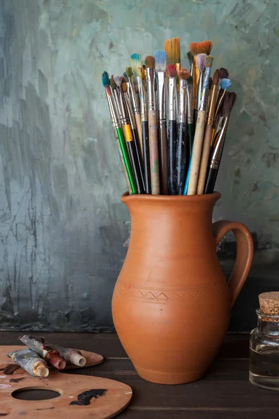 Paintbrushes in a jug from potters clay, palette, paint tubes an