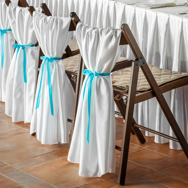 Row of wedding chairs, decorated with white fabric and blue ribb