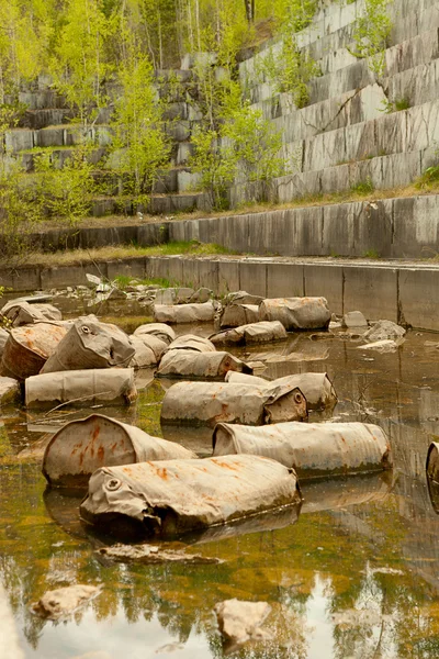 Old marble quarry, abandoned fuel barrels on bottom. Careless attitude towards nature. Industrial waste products of oil refining. Extraction of minerals by open method.