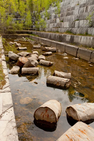 Old marble quarry, abandoned fuel barrels on bottom. Careless attitude towards nature. Industrial waste products of oil refining. Extraction of minerals by open method.