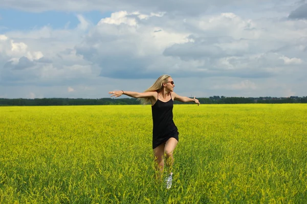 Happy woman in black dress  jumps to the sky in the yellow meadow at the summer day.