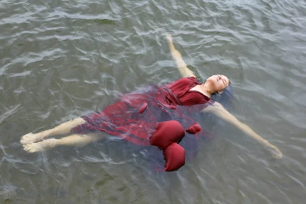 Young beautiful drowned woman in red dress lying in the water outdoor
