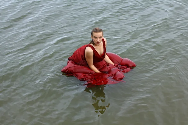 Attractive girl have fun, dives and drowned at the sea water. Woman portrait with red dress.