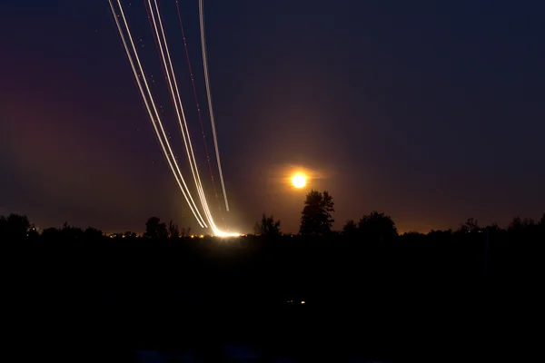 Passenger planes take off from runways against beautiful night sky with moon. Long exposure. Motion blur, and light trace