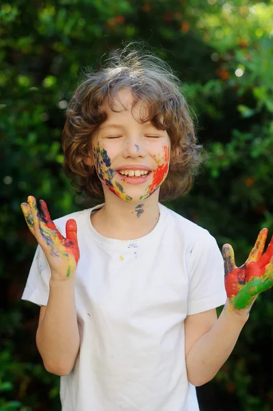 Child laughs, his face and hands in the paint