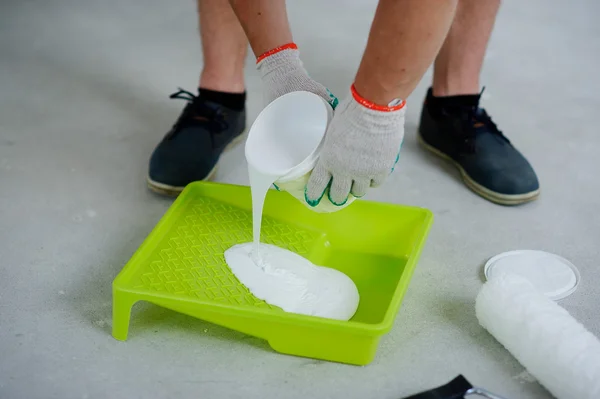 The person pours white paint in a tray.